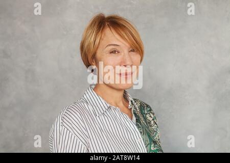 Fröhliche reife Frau auf grauem Hintergrund Stockfoto