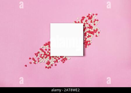 Weißer Papierblock und herzförmige Bonbons auf pinkfarbenem Hintergrund. Liebe oder Valentinstag Konzept. Stockfoto