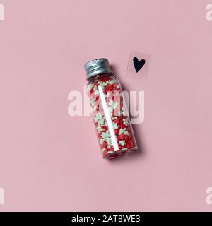Eine Flasche mit herzförmigen Bonbons und Liebessymbol auf pinkfarbenem Hintergrund. Liebe oder Valentinstag Konzept. Stockfoto