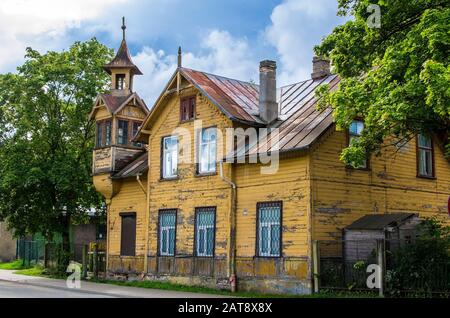 Altes gelbliches Holzhaus mit kleinem Turm während des Sonnentags im Sommer in Riga, Lettland. Traditionelle Lettische Holzarchitektur. Stockfoto