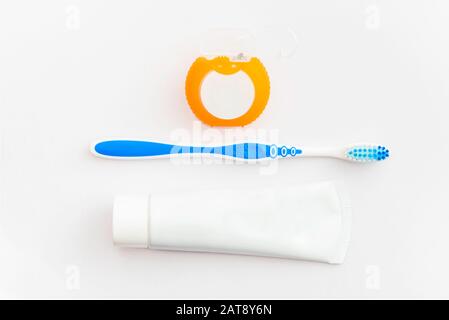 Orangefarbene Zahnseide mit blauer Zahnbürste und weißer Zahnpasta Stockfoto