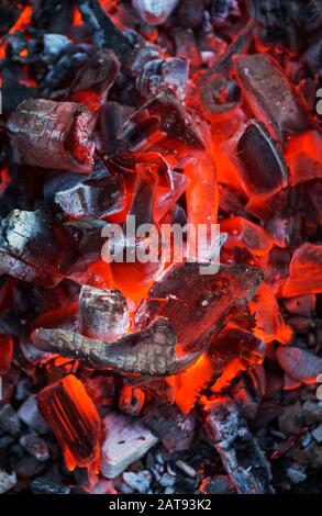 Brennende Kohlen. Verfallende Holzkohle. Textur Glut Nahaufnahme. Glühende Glut. Feuerstelle mit glühender Kohle. Live-Kohleverbrennung. Hintergrund. Stockfoto