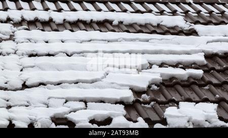 Auf den Dachziegeln taut Schnee. Malerischer Winterwetterhintergrund. Ein schneebedecktes Dach, auf das eine Dachlawine abging. Stockfoto