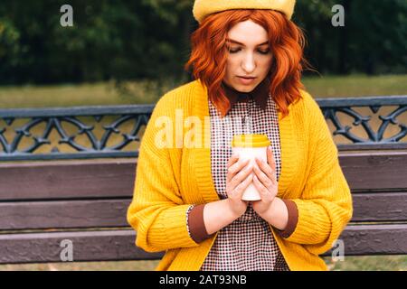 Eine Frau sitzt auf einer Parkbank und Halten einer Bambus Schale mit heißem Kaffee Stockfoto