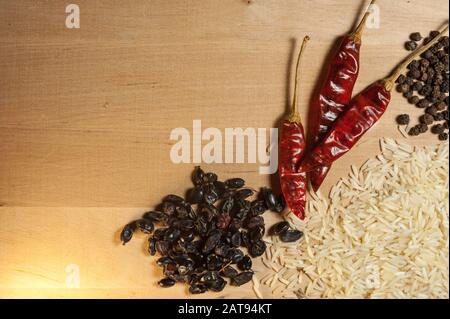 Getrocknete Barbeere, rote Paprika und schwarzer Pfeffer mit Reis auf einem Holzbrett Stockfoto