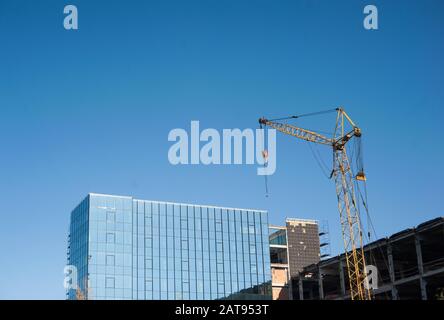 Der gelbe Turmkran baut ein Glasgebäude gegen einen blauen Himmel Stockfoto