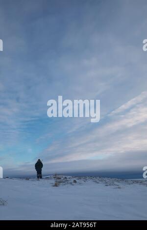 Mann im Winter Kleidung stehen auf Schnee beobachten das Wetter auf Tundra Landschaft, während eine Gewehr, in der Nähe von Arviat, Nunavut, Kanada Stockfoto
