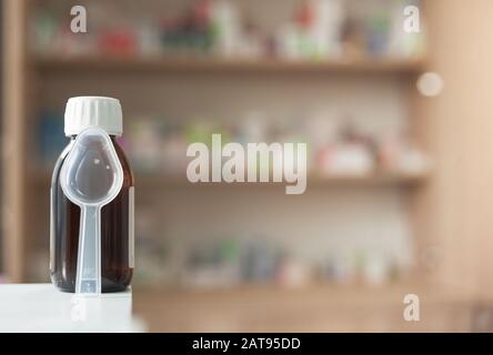 Medikamente in einer dunklen Glasflasche mit einem Messlöffel vor dem Hintergrund anderer Medikamente in einer Apotheke Stockfoto