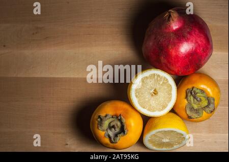 Reifer Granatapfel, Zitrone und Persiflage auf einem Holzbrett Stockfoto