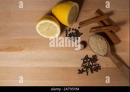 Gewürze für Glühwein auf Holzbrett: Zitrone, brauner Zucker, Muskatnuss, Zimt, Nelken, schwarzer Pfeffer Stockfoto