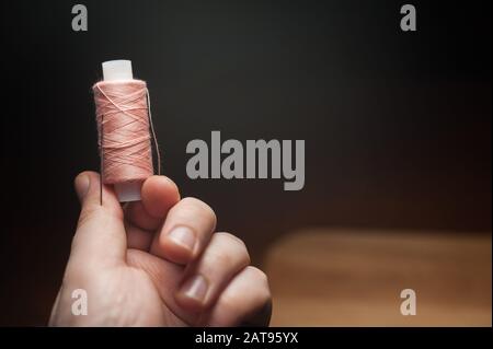 Spule aus rosafarbenem Faden mit einer Nadel in der Hand auf dunklem Hintergrund Stockfoto