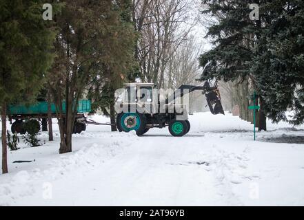 Traktor mit Anhänger im Winter im botanischen Garten befreit die Straße von Schnee und Ästen. Vorlage für das Design. Kopierbereich. Stockfoto