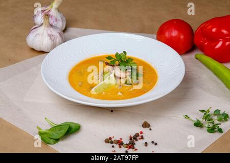 Käsesuppe mit Garnelen. Gelbe Suppe ist mit Zitrone und Petersilie verziert. Weiße runde Platte liegt auf einem weißen und grauen Wickelpapier, überlagert mit Pep Stockfoto