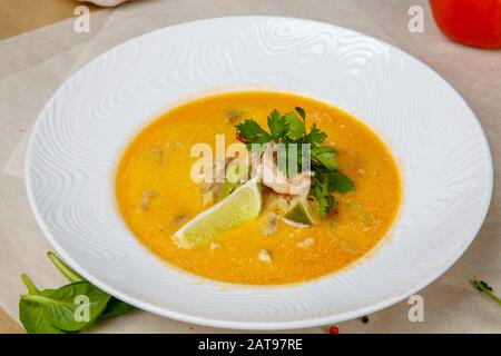 Käsesuppe mit Garnelen. Gelbe Suppe ist mit Zitrone und Petersilie verziert. Weiße runde Platte liegt auf einem weißen und grauen Wickelpapier, überlagert mit Pep Stockfoto