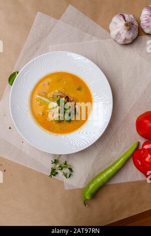 Käsesuppe mit Garnelen. Gelbe Suppe ist mit Zitrone und Petersilie verziert. Weiße runde Platte liegt auf einem weißen und grauen Wickelpapier, überlagert mit Pep Stockfoto