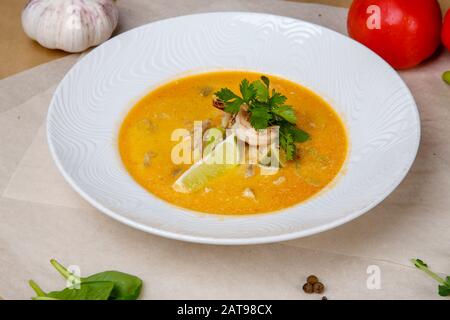 Käsesuppe mit Garnelen. Gelbe Suppe ist mit Zitrone und Petersilie verziert. Weiße runde Platte liegt auf einem weißen und grauen Wickelpapier, überlagert mit Pep Stockfoto