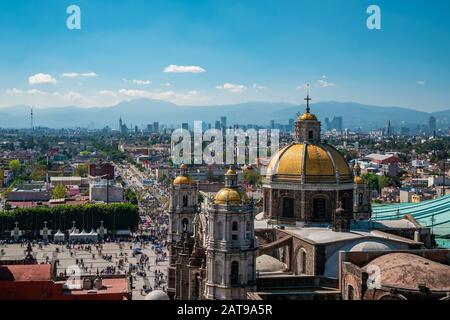 Mexiko-Stadt, Mexiko, die Basilika Unserer Lieben Frau von Guadalupe mit der Skyline von Mexiko-Stadt im Hintergrund. Stockfoto