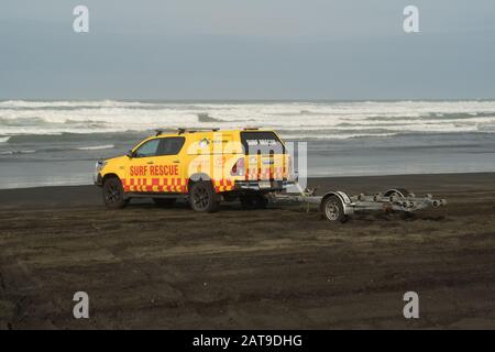 Surf Rescue 4WD Truck am schwarzen Sandstrand mit Jet-Skiboot Trailer Seewellen Himmel Hintergrund muriwai Strand, Auckland, Neuseeland Stockfoto