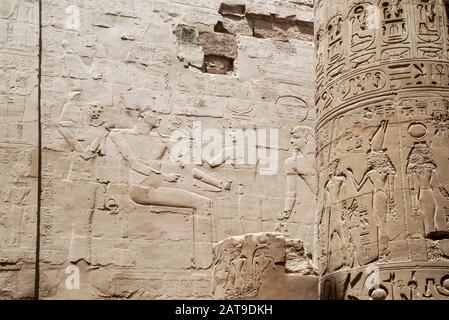 Luxor, Karnak, Ägypten, Afrika. Tempel von Karnak. Detail der Reliefschnitzereien eines Mannes und einer Frau an der Wand und der Hieroglyphen an der Säule. Stockfoto