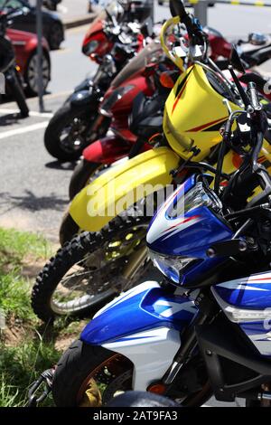 Motorrad: Bunte Fahrräder hintereinander, draußen in der Stadt an einem warmen hellen Tag geparkt. Vertikales Farbbild im Hochformat. Stockfoto