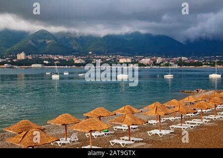 Abend in der Gelendzhik Bay. Im Vordergrund steht ein Kieselstrand, Sonnenliegen und Strohschirme aus der Sonne. In der Bucht auf dem Parkplatz des YA Stockfoto