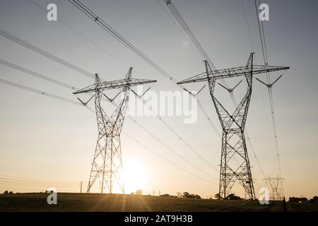 Landschaft von australischen Hochspannungsleitungen mit Sonnenuntergang im Hintergrund. Stockfoto