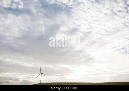 Eine Windkraftanlage, die in der Energieerzeugung auf einem Hügel mit untergehenden Sonne verwendet wird Stockfoto