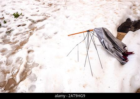 Regenschirm zerbrochen durch den Wind, der auf dem Boden einer verschneiten Straße liegt. Stockfoto
