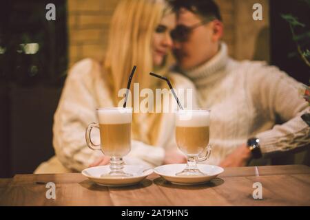 Junges glückliches Paar verliebt sich in Café, Mann und Frau lächeln zusammen umarmend und trinken Kaffee. Ein Paar Spricht Im Winter Im Café. Glückliches Paar, das einen genießt Stockfoto