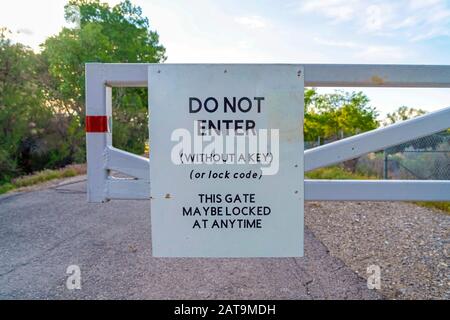 Nicht betreten Schild an einem weißen Tor gegen Straßenbäume und bewölkten Himmel montiert Stockfoto