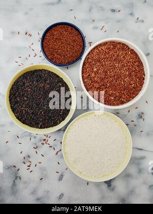 Keramikschüsseln mit einer Vielzahl von Getreide und Reis, einschließlich rotem Quinoa, rotem Reis, schwarzem Reis und weißem Reis auf einer Marmorplatte. Stockfoto