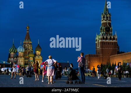 Menschen, die während des Sonnenuntergangs im Sommer auf dem Roten Platz mit der Kathedrale von Saint Basil und dem Turm von Spasskaya aus dem Kreml spazieren gehen Stockfoto