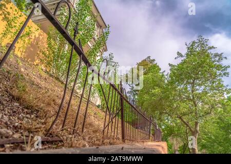 Beschädigter und rostiger Eisenzaun gegen weiße Baubäume und bewölkten Himmel Stockfoto