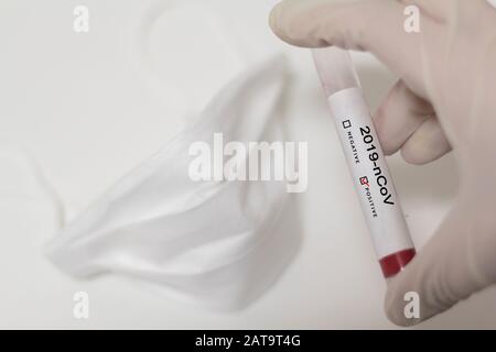 Draufsicht der Gesichtsmaske und der Hand, die Coronavirus Bluttest mit positivem Ergebnis hält Stockfoto