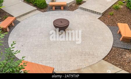 Panorama Luftaufnahme von Bänken und Feuerstelle auf kreisförmiger gepflasterter Terrasse außerhalb eines Gebäudes Stockfoto