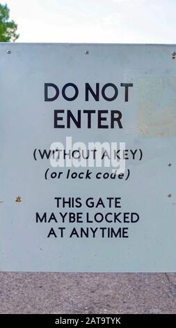 Vertikal nicht betreten Schild auf einem weißen Tor gegen Straßenbäume und bewölkten Himmel montiert Stockfoto