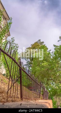 Vertikaler Rahmen beschädigt und rostig Eisenzaun gegen weiße Baubäume und bewölkten Himmel Stockfoto