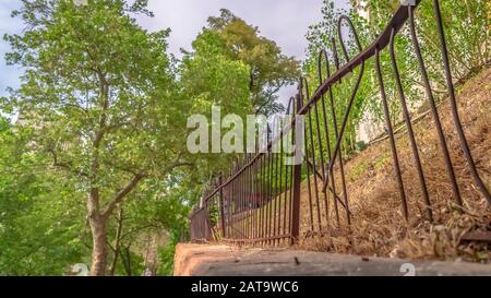 Panorama beschädigt und rostig Eisenzaun gegen weiße Baubäume und bewölkten Himmel Stockfoto