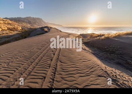 Herrlicher Sonnenuntergang über dem Wasser Blick auf die chilenische Küste. Eine idyllische Strandlandschaft mit dem Sonnenlicht, das die Sanddünen mit orangen Farben erhellt Stockfoto