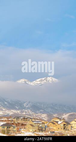 Foto Vertikaler Rahmen Snowy Mountain teilweise von dicken Wolken mit Häusern im Vordergrund bedeckt Stockfoto