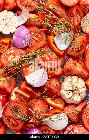 Rohe rote Tomate, in Scheiben geschnitten, lila Zwiebel, Knoblauch und Thymian, die im Ofen geröstet werden können, als Hauptzutat für geröstete Tomatensuppe, Draufsicht, Nahaufnahme, Stockfoto