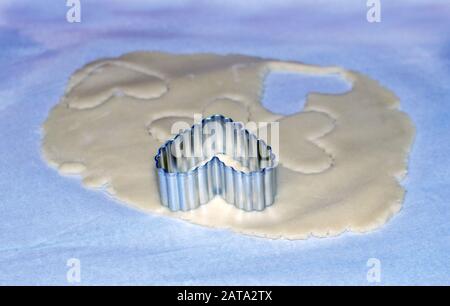 Herzen, die mit diesem Metallkeksschneider aus Teig gestempelt wurden, werden köstliche Plätzchen herstellen Stockfoto