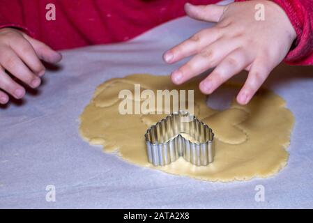 Kleine Hand stempelt Herzen in Plätzchenteig aus Stockfoto