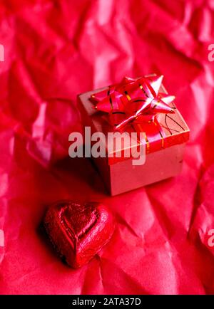 Kleine Geschenkbox mit einem Ring im Inneren und einer roten Folie umhülltes Schokoladenherz Stockfoto