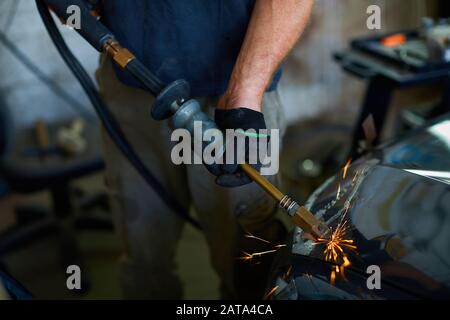 Ein Mitarbeiter der Karosserielackiererei beseitigt einen kleinen Metalldefekt mit einem speziellen Handwerkzeug Stockfoto