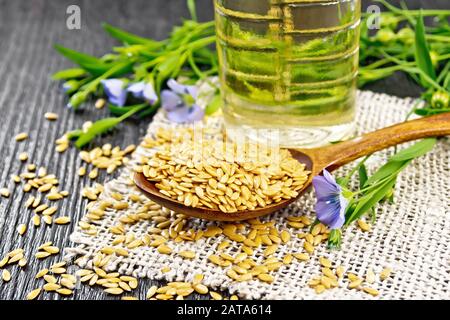 Weiße Leinensamen im Löffel, Flachsstängel mit blauen Blumen und grünen Blättern auf dem Boden, Öl in einer Flasche auf Holzbrettgrund Stockfoto