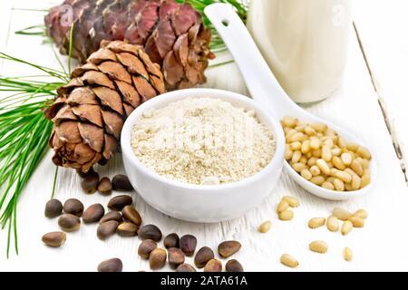 Zedernmehl in einer Schüssel, Nüsse und Kegel, Löffel mit geschälten Nüssen, grüner Kiefernzweig und Zedernmilch in einer Flasche auf dem Hintergrund von hellem Holzbrett Stockfoto