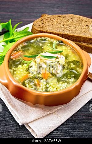 Schweinerippensuppe mit Couscous und Spinat in einer Tonschale auf Küchentuch, Brot auf Holzbretthintergrund Stockfoto