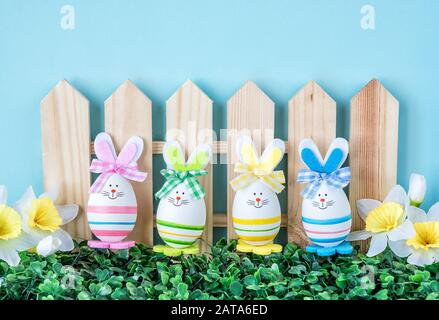 Mehrere lustige Osterhasen mit bunten Schleifen aus Ostereiern stehen auf einem grünen Gras mit Blumen, gegen den blauen Himmel, mit Platz für Text Stockfoto