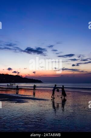 Menschen am Strand in Jimbaran Bay, Bali, bei Sonnenuntergang Stockfoto